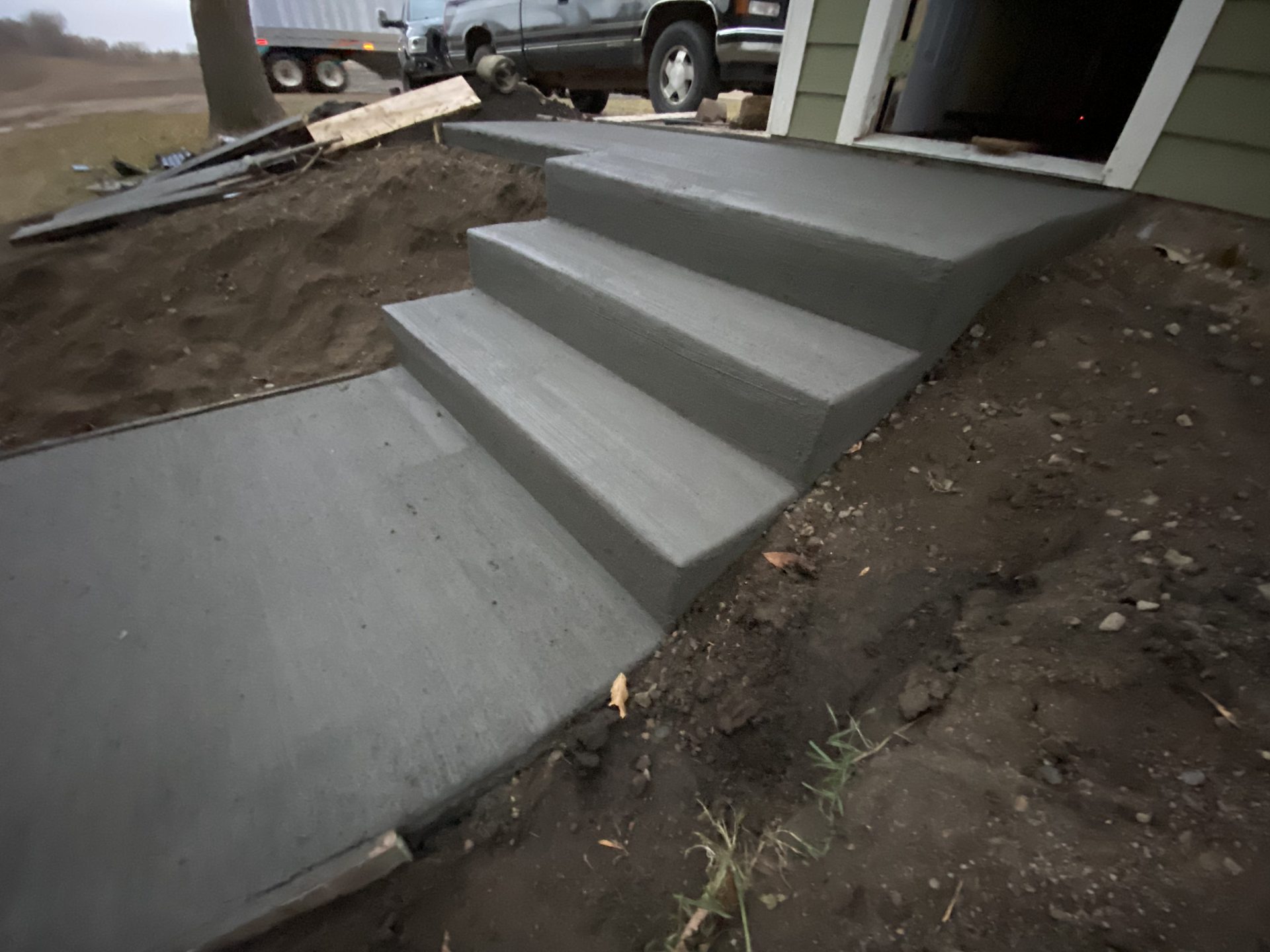 Newly poured concrete steps and landing leading to residential garage entrance, with surrounding dirt grading.