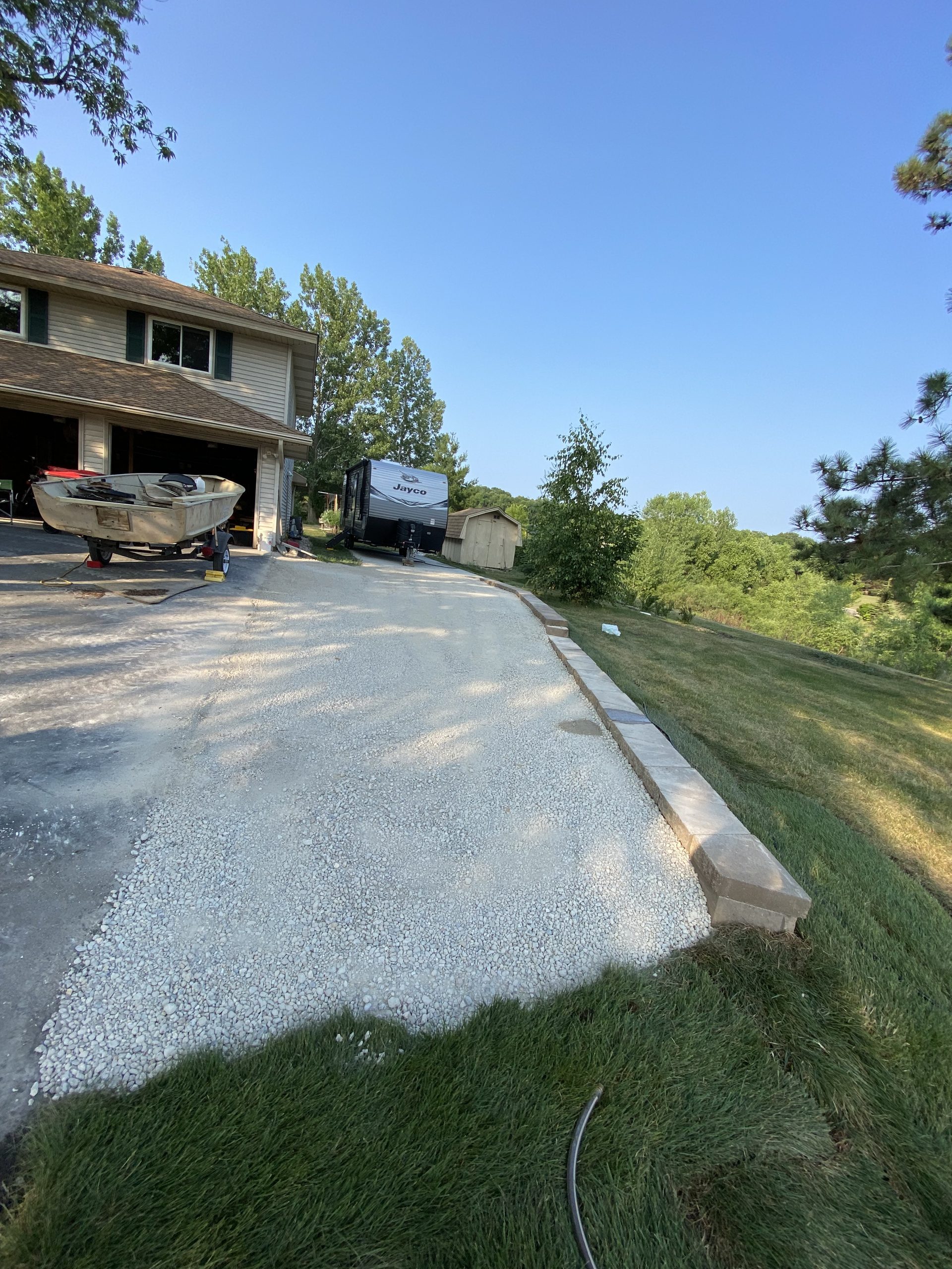 Newly installed gravel driveway with concrete edging and retaining wall, bordered by green lawn and trees.