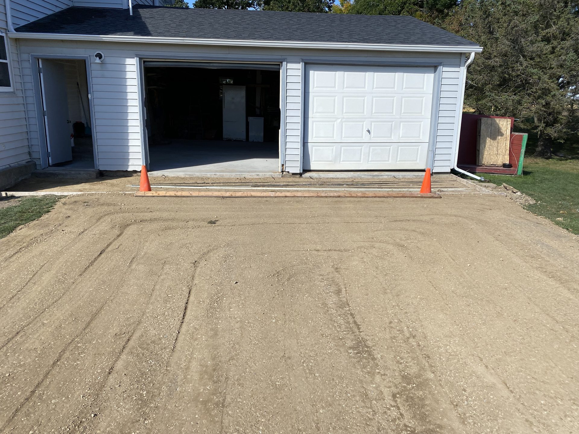 Gravel base preparation showing base materials and safety markers in front of two-car garage.