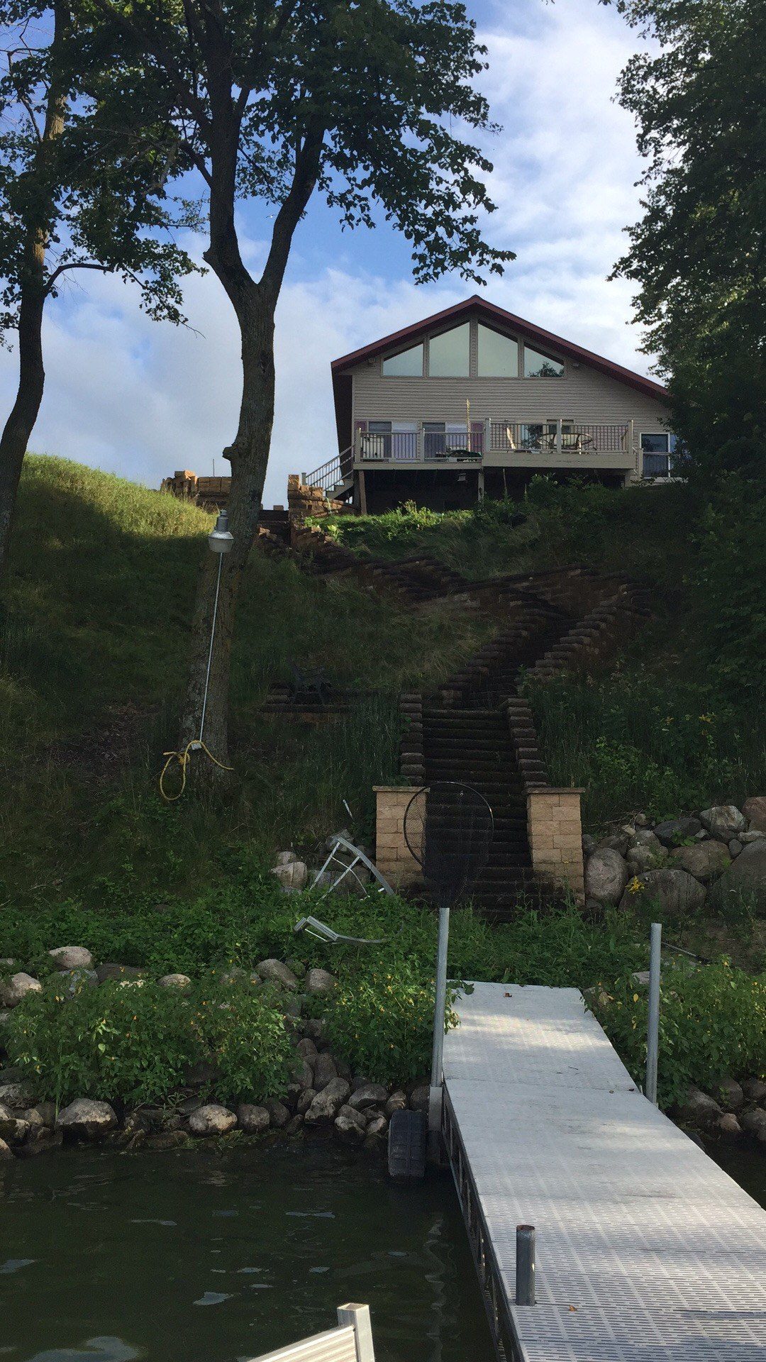 Finished residential home on elevated foundation overlooking water, with composite deck, stone landscaping, and mature trees.