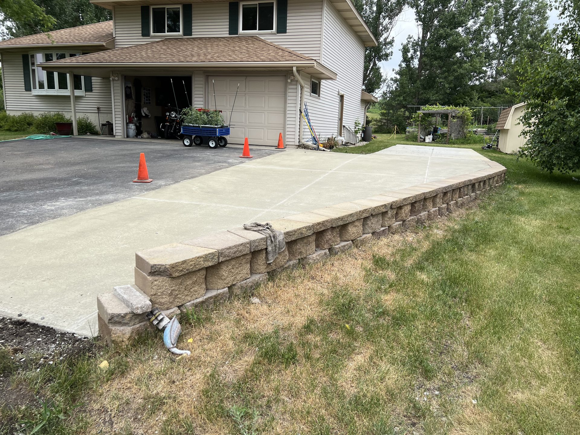 New concrete patio with stone retaining wall adjacent to residential driveway.