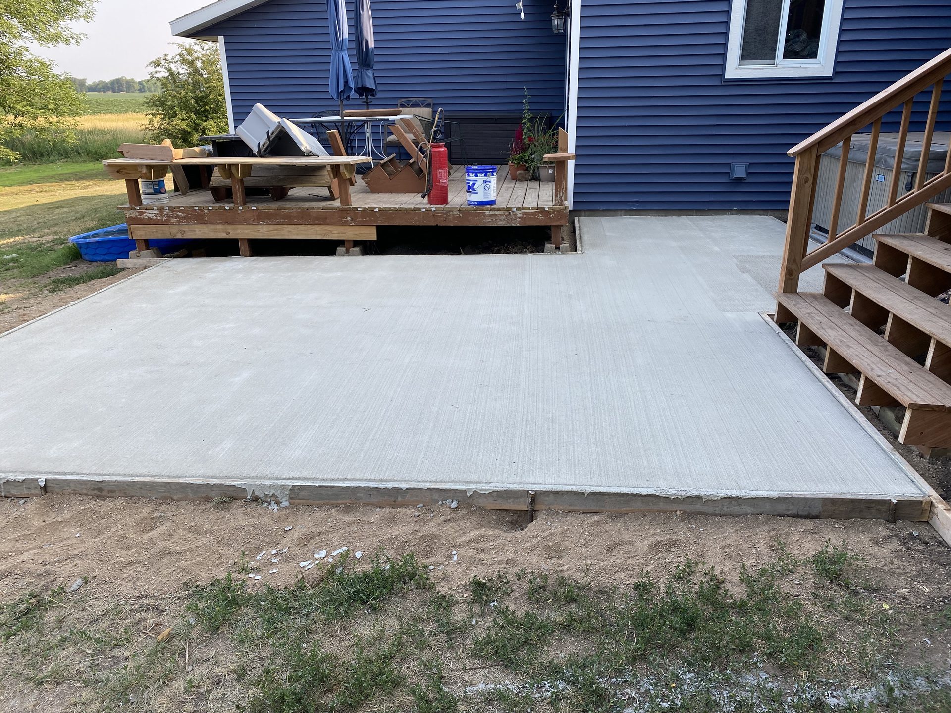 Newly poured concrete patio pad adjacent to wooden deck and blue siding home.