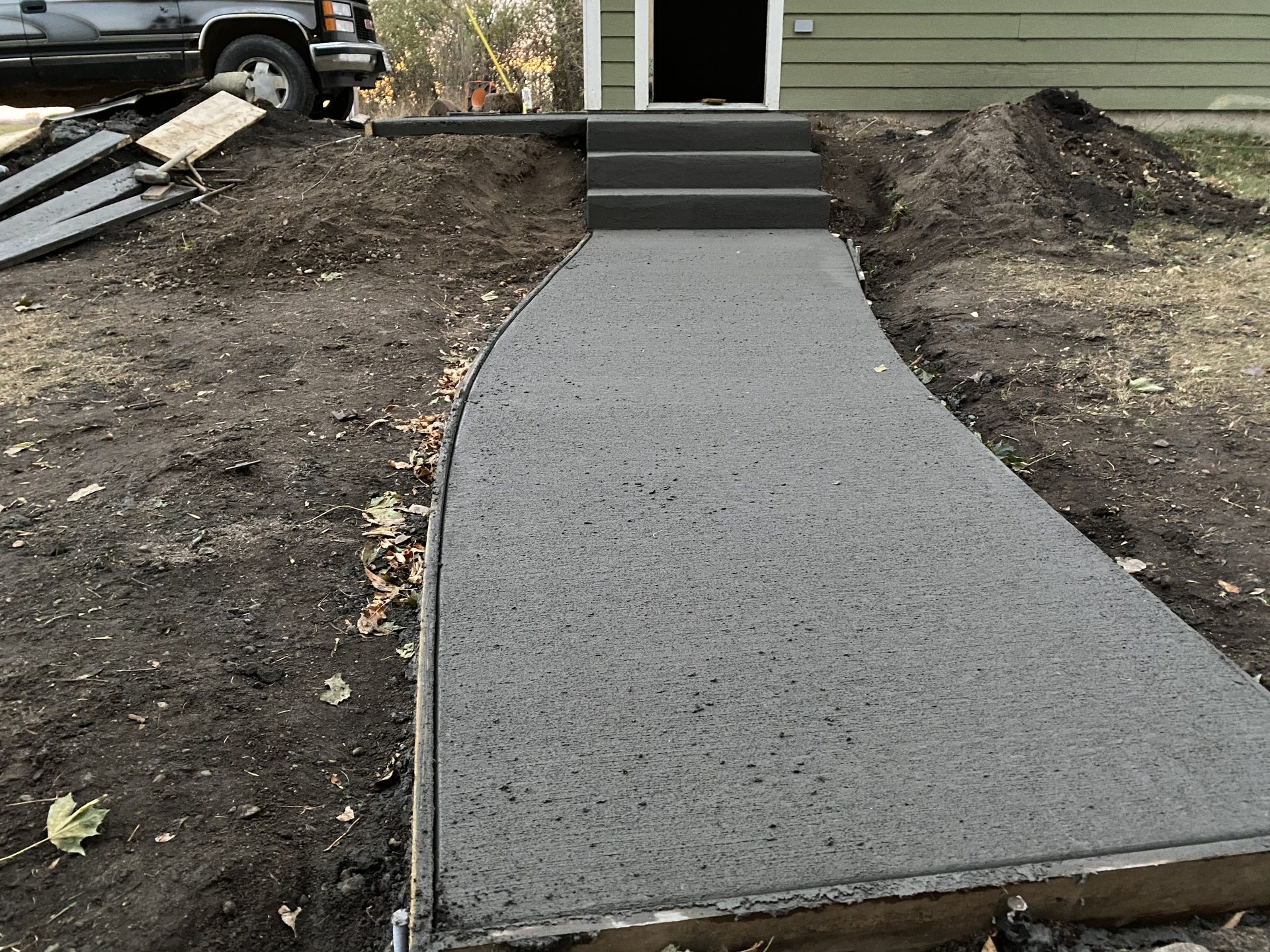 Newly installed concrete walkway with black metal steps leading to residential entrance.
