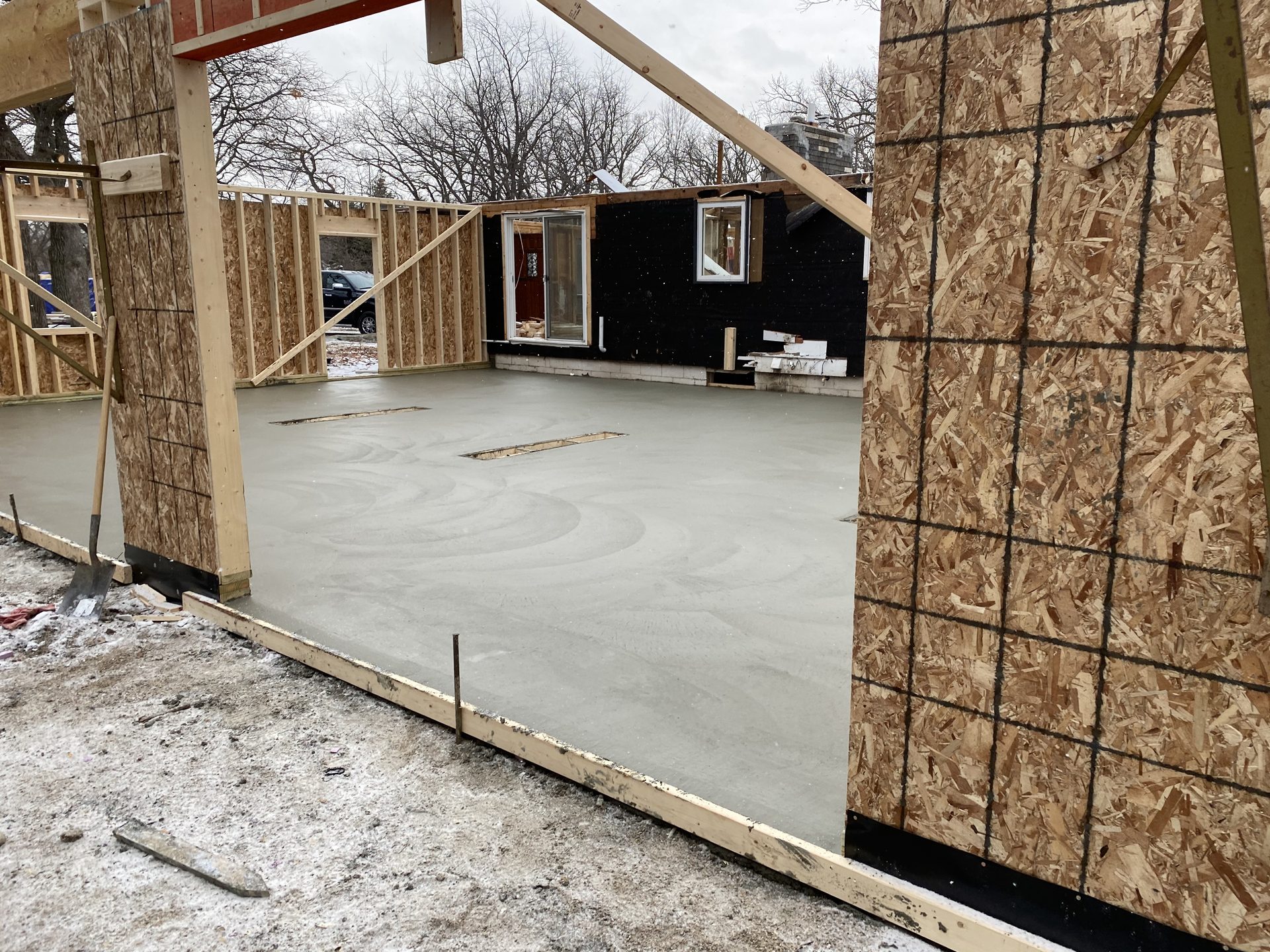 Fresh concrete foundation pour for residential construction with wooden framing and OSB sheathing visible.