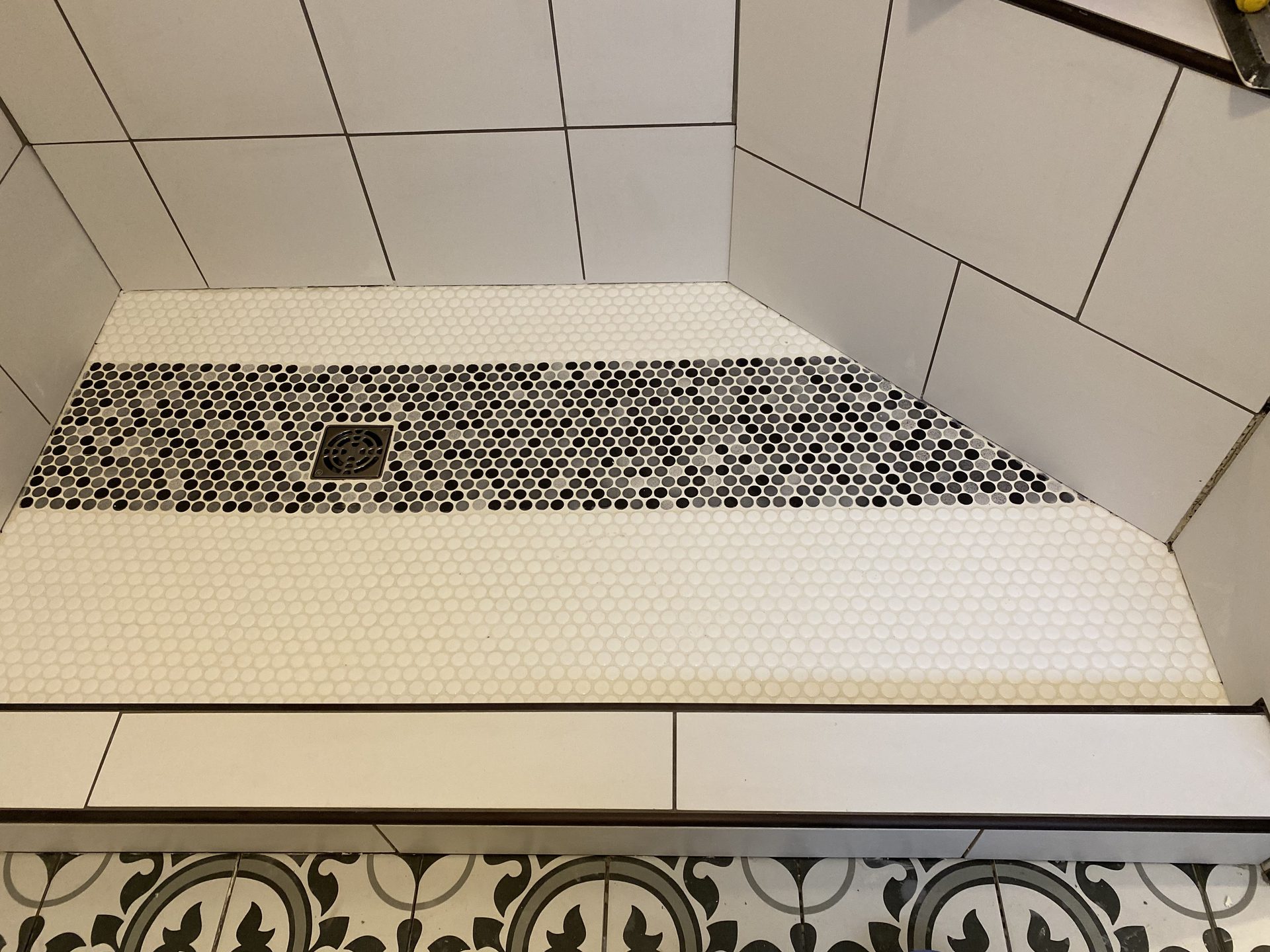 Completed tile shower floor with black and white penny tile pattern and integrated drain.